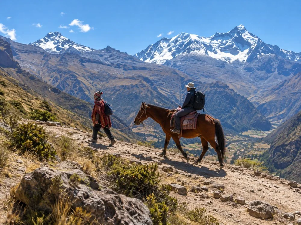 A local handler leading a saddled horse with a rider up the dusty trail